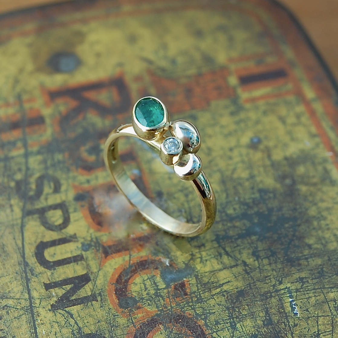 Oval emerald set in gold cup setting with diamond and gold cluster detail