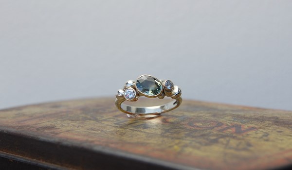 Pale green sapphire set in yellow gold cup setting with diamonds and white gold clusters on white gold ring