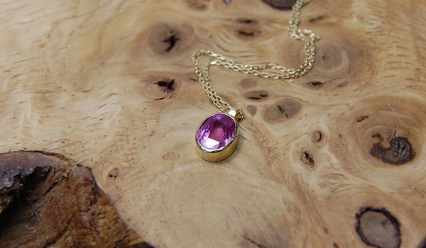 Oval pink sapphire set in 18ct yellow gold rub-over setting on 18inch curb chain