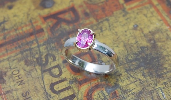 Oval pink sapphire set in 9ct yellow gold claw setting on a white gold band