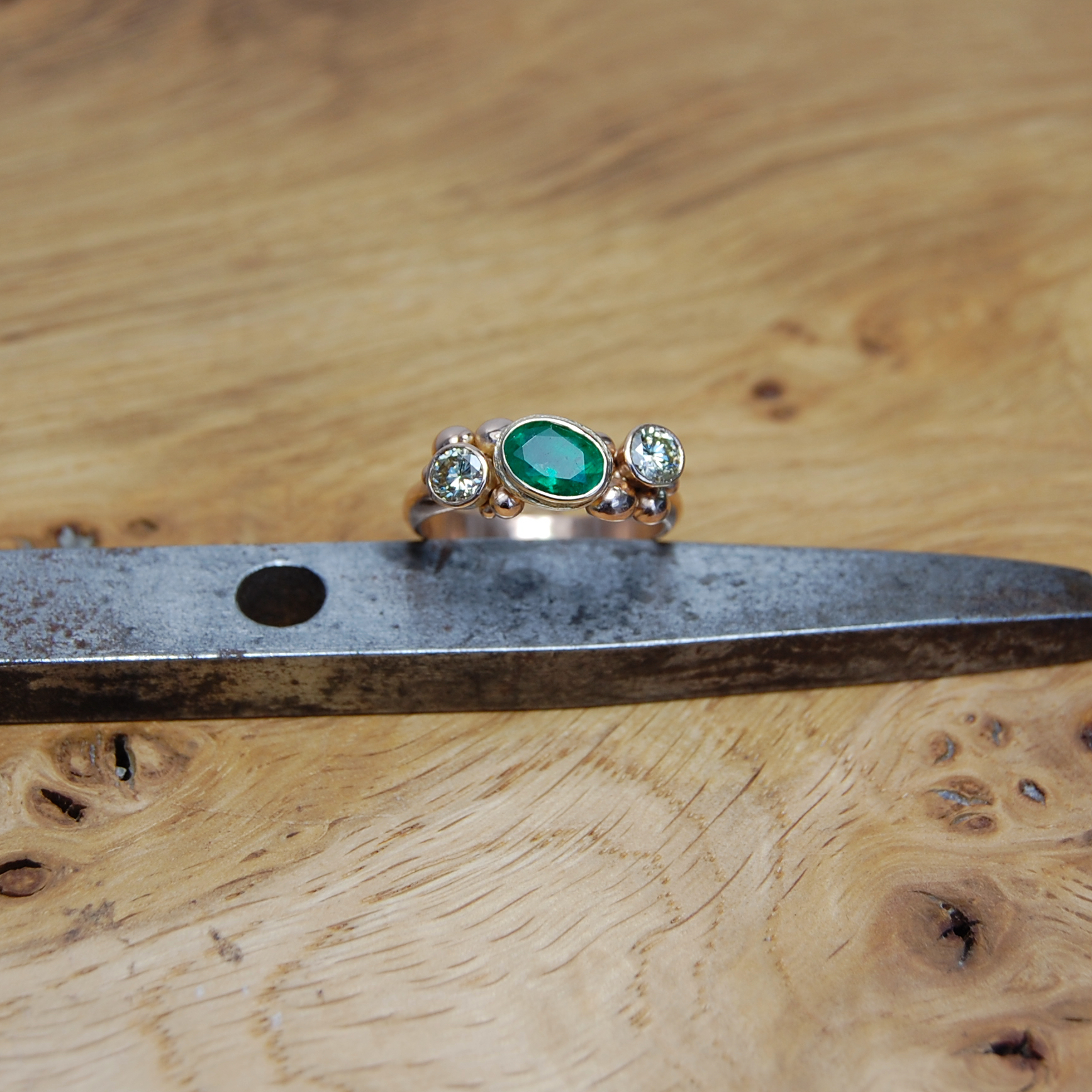 Oval emerald set in yellow gold cup setting with diamonds and rose gold clusters ring